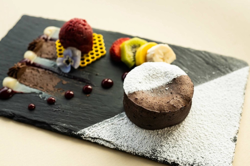 Chocolate dessert dusted with icing sugar, served with sorbet and fresh fruit on slate