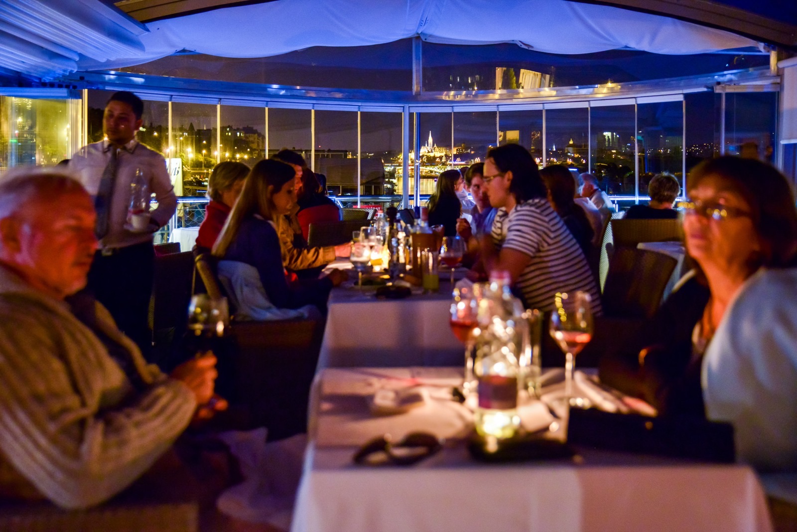 Guests at dinner, the lit embankment behind them
