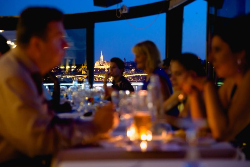 Guests on the panoramic terrace, the lit Buda side behind them
